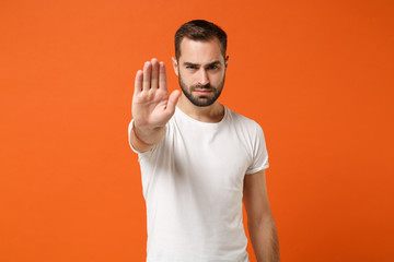 Serious young man in casual white t-shirt posing isolated on orange wall background studio...