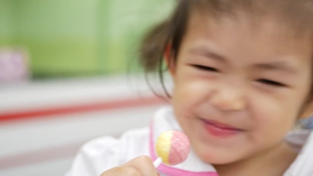 Little Asian baby girl enjoys having / licking / sucking her lollipop, a hard candy mounted on a stick