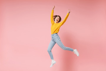 Fototapeta na wymiar Cheerful young brunette woman girl in yellow sweater posing isolated on pastel pink background in studio. People lifestyle concept. Mock up copy space. Having fun fooling around rising hands, jumping.