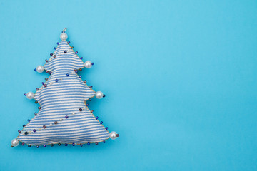 Handmade striped textile fabric naive retro style Christmas tree ornament decorated with beads on blue background with space for text