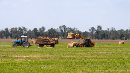 Tractor loading hay bales on truck agricultural works