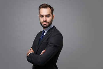 Side view of young business man in classic black suit shirt tie posing isolated on grey background. Achievement career wealth business concept. Mock up copy space. Hold hands crossed, looking camera.