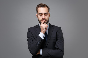 Young business man in classic black suit shirt tie posing isolated on grey background. Achievement career wealth business concept. Mock up copy space. Put hand prop up on chin, keeping eyes closed.