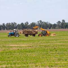 Tractor loading hay bales on truck agricultural works