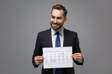 Smiling young bearded business man in classic black suit shirt tie posing isolated on grey wall...