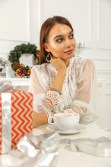 Slim young woman with wooden table and free space for your decoration. Xmas home interior and cup of coffee in hands.Box of xmas gifts and silver ribbon. 