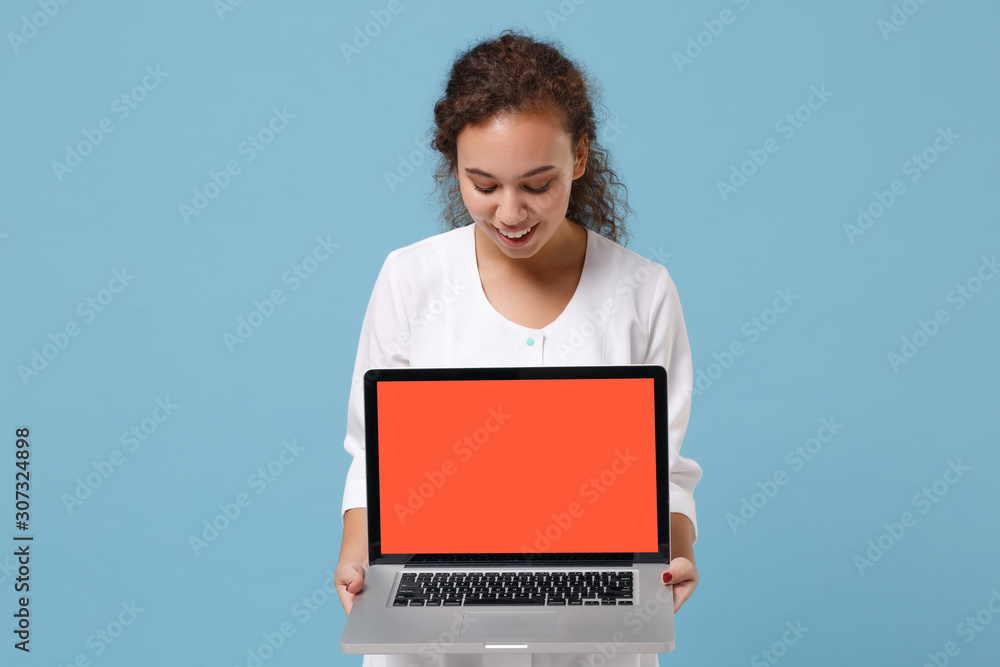 Wall mural Pretty african american doctor woman isolated on blue background. Doctor in medical gown holding laptop pc computer with blank empty screen. Healthcare personnel medicine concept. Mock up copy space.