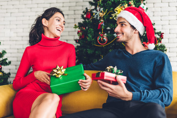 Obraz na płótnie Canvas Romantic sweet couple in santa hats having fun decorating christmas tree and smiling while celebrating new year eve and enjoying spending time together.man giving gift box surprise to woman 