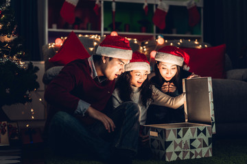 Portrait of happy family father and mother with daughter in santa hats having fun opening magic...