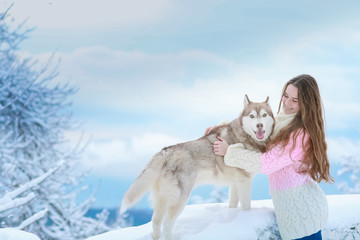 A woman with a husky dog walking on winter snow-covered mountains.