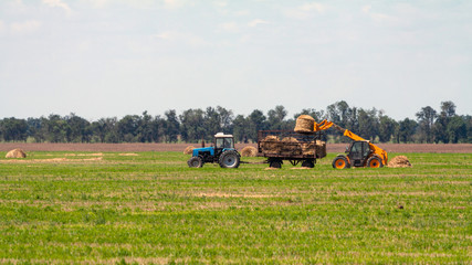 Tractor loading hay bales on truck agricultural works