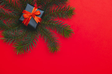 Top view of Christmas gift box red balls with spruce branches, pine cones, red berries and bell on red background.