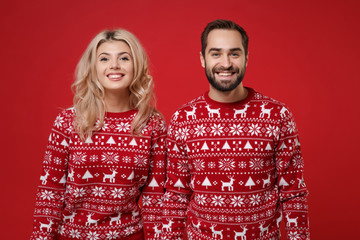 Merry young couple guy girl in Christmas knitted sweaters posing together isolated on bright red background studio portrait. Happy New Year 2020 celebration holiday party concept. Mock up copy space.
