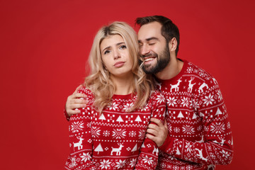 Confused young couple guy girl in Christmas knitted sweaters posing together isolated on red wall background studio portrait. Happy New Year 2020 celebration holiday party concept. Mock up copy space.