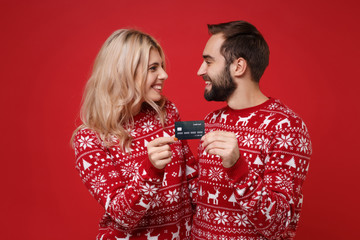 Pretty young couple guy girl in Christmas knitted sweaters posing isolated on bright red...