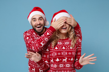 Excited young couple guy girl in Christmas sweaters, Santa hat posing isolated on blue background. Happy New Year 2020 celebration holiday party concept. Mock up copy space. Covering eyes with hands.