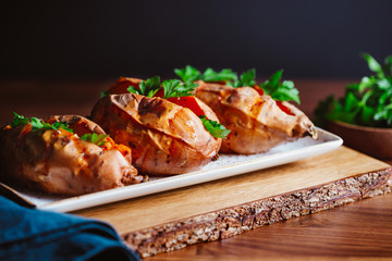 Baked three sweet potatoes with fresh parsley on a white ceramic dish. Healthy veggie dinner or lunch.