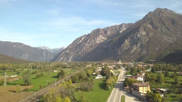 Aerial view of a small historic town Venzone in Northern Italy with red tiled roofs of old buildings and majestic Alps mountains.