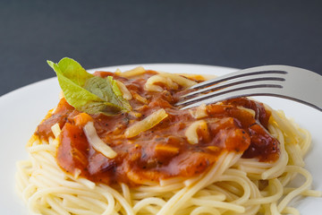 View of spagetti bolognese with green basil on top over black background. Silver fork placed on top of the dishes.