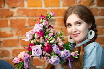 Beautiful girl with a bouquet of flowers on a brick wall background