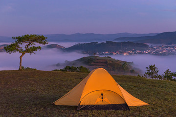 Glowing tent on the hill with misty valley landscape