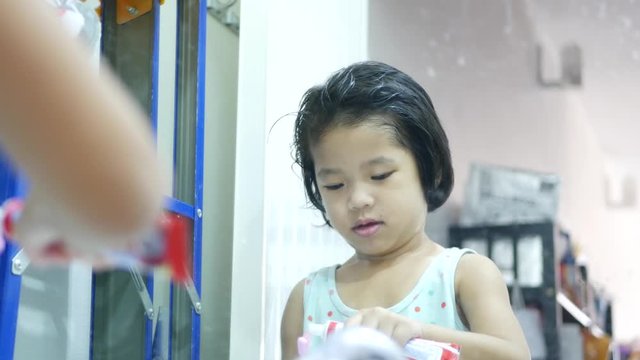 Little Asian baby girl, 3 years old, learning to squeeze out the toothpaste onto her toothbrush and close the cap by herself - baby's fine motor learning for hand strength