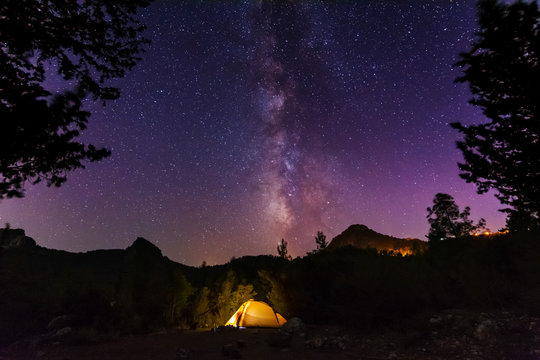 Vertical landscape images with a night starry sky and a milky way against the backdrop of a yellow tourist tent, which is highlighted from the inside.