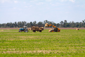 Tractor loading hay bales on truck agricultural works