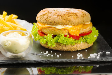pork burger with ketchup and french fries. wooden board on black background