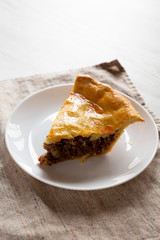 Slice of Homemade Canadian Tourtiere Meat Pie on a white plate , side view. Copy space.