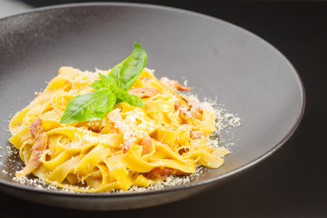 pasta with ham, bacon and cheese in a black plate