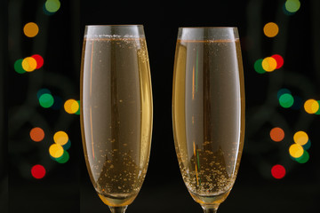 Two glasses with champagne with festive lights on a dark background.