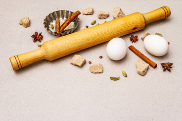 Christmas cooking background, spices, eggs, brown lump sugar, cupcake baking dish and a rolling pin. Light stone concrete background