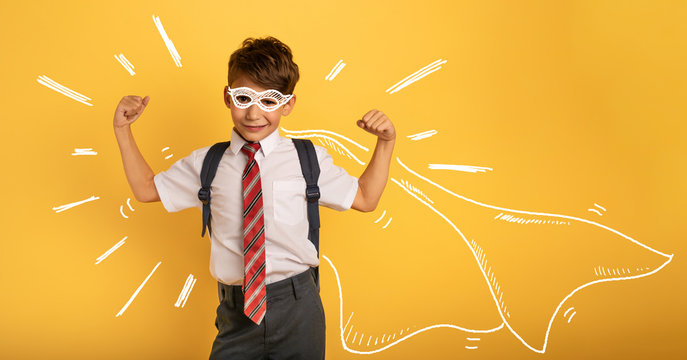 Young boy student acts like a super hero. Yellow background