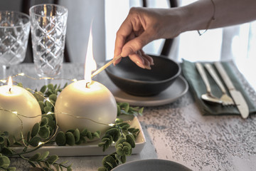 Female hand light a candle at Nordic Festive table for Christmas or New Year celebration.