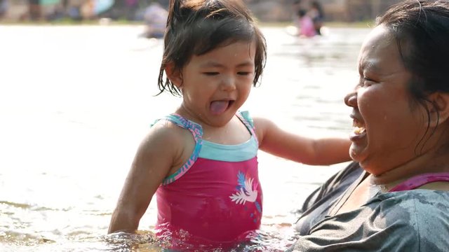 Little Asian baby girl, 25 months old, enjoys playing water in a river with her auntie - playing outdoor and engaging with nature provides positive impact on baby's health and development