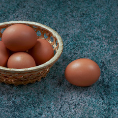 several fresh chicken eggs in a straw basket on a wooden background. Healthy eating concept.
