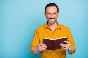 Portrait of positive cheerful man enjoy weekends he spend on reading holding paper book wear casual...