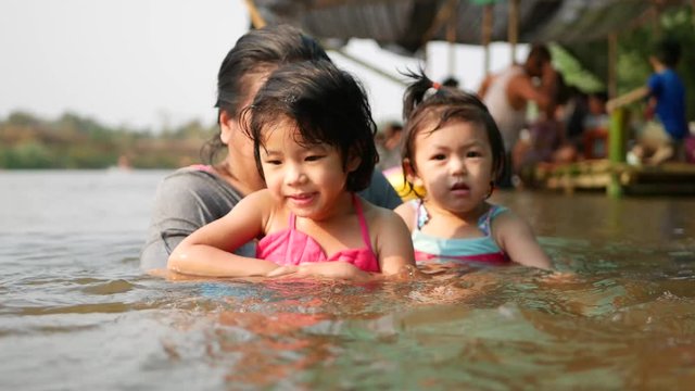 Two little Asian baby girls, sisters, enjoys playing water in a river with her auntie - playing outdoor and engaging with nature provides positive impact on baby's health and development