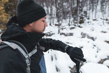 Fototapeta na wymiar Young hiker man in black outfit checking time and health indicators on smartwatch in rest time, adjusting his GPS watch before outdoor sports activity; trekking in snowy winter day with equipment