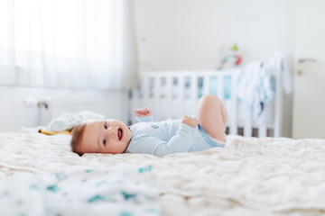 Side view of adorable chubby six months old baby boy lying on bed, smiling and looking at camera....