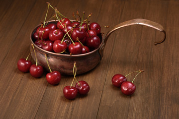 rustic copper ladle with sweet cherry on a wooden background