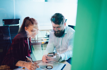 Adult male and female workers sitting in meeting room using mobile in company