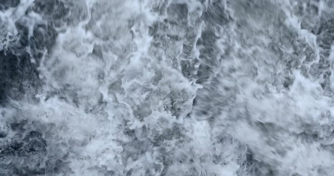 A river streaming heaviliy water waves current movement winter autumn dark mood flowing fast splashing foaming on a cold day late autumn leaves falling into the water filmed in 4k with a film camera