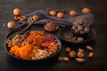 Mix of dried fruits, energy bites, chocolate paste and nuts on a black table. Low key