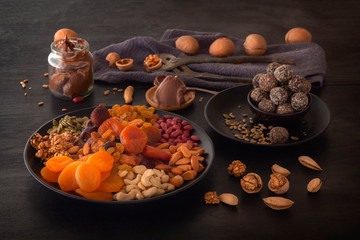 Mix of dried fruits, energy bites, chocolate paste and nuts on a black table. Low key
