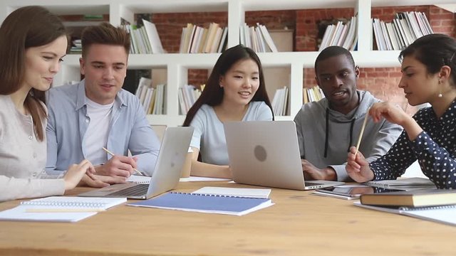 Happy focused diverse students working in groups on computers.