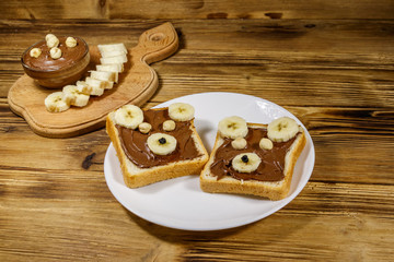 Obraz na płótnie Canvas Two sweet sandwiches with delicious chocolate hazelnut spread and banana in shape of bear on wooden table