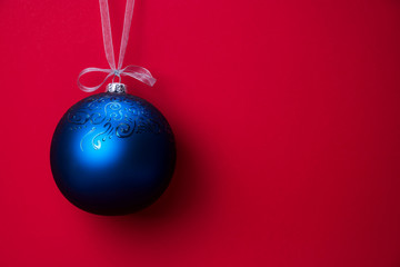 Christmas ball hanging on a ribbon over red background. Copy space.