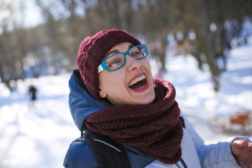 A woman wearing glasses dressed in warm clothes smiles and laughs.